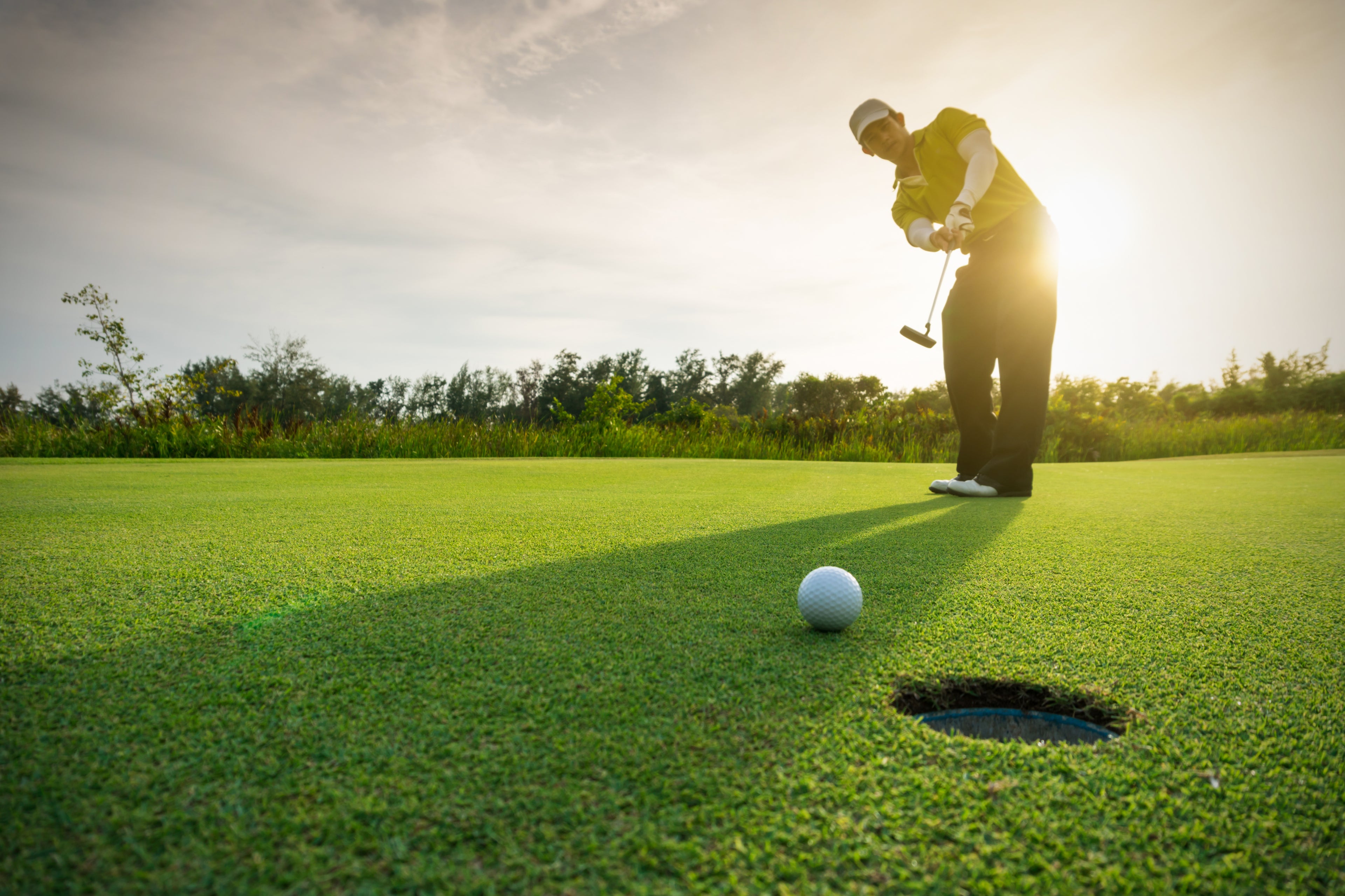 Golfer taking a putt on a green with a sunset in the background in the Island of Mauritius